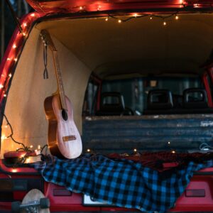 A serene camping scene with an acoustic guitar and lights in a car trunk, perfect for music lovers.