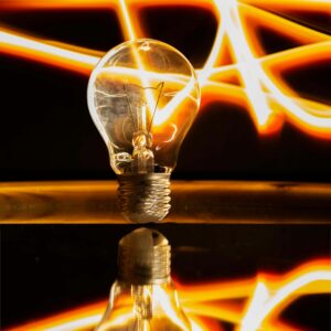 Close-up of an illuminated light bulb with neon light streaks and reflection, exuding energy and creativity.