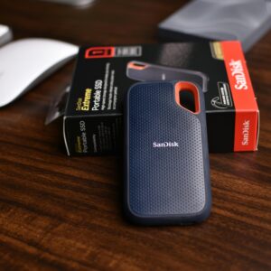 Close-up of a SanDisk portable SSD with a box and mouse on a wooden desk, ideal for tech-related themes.