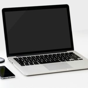 A minimalist workspace featuring a laptop, smartphone, and an apple on a clean white desk.